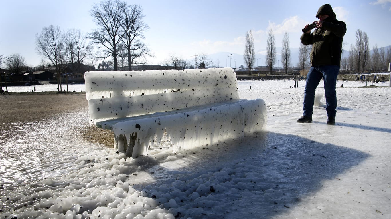 Schweiz, Yverdon-Les-Bains: Ein Mann fotografiert eine zugefrorene Bank am Neuenburgersee: Die Kältewelle hat weite Teile Europas im Griff.