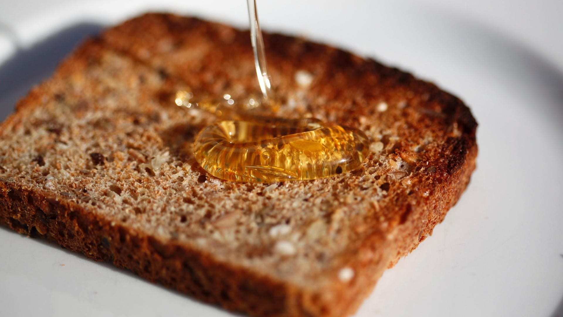 Honig tropft auf eine Scheibe Toast: Mehr als ein Kilo Honig isst jeder Bundesbürger im Schnitt pro Jahr. Das Geschäft mit dem beliebten Bienenprodukt lockt aber auch schwarze Schafe an. Sie panschen aus Profitgründen.