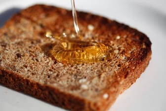 Honig tropft auf eine Scheibe Toast: Mehr als ein Kilo Honig isst jeder Bundesbürger im Schnitt pro Jahr. Das Geschäft mit dem beliebten Bienenprodukt lockt aber auch schwarze Schafe an. Sie panschen aus Profitgründen.
