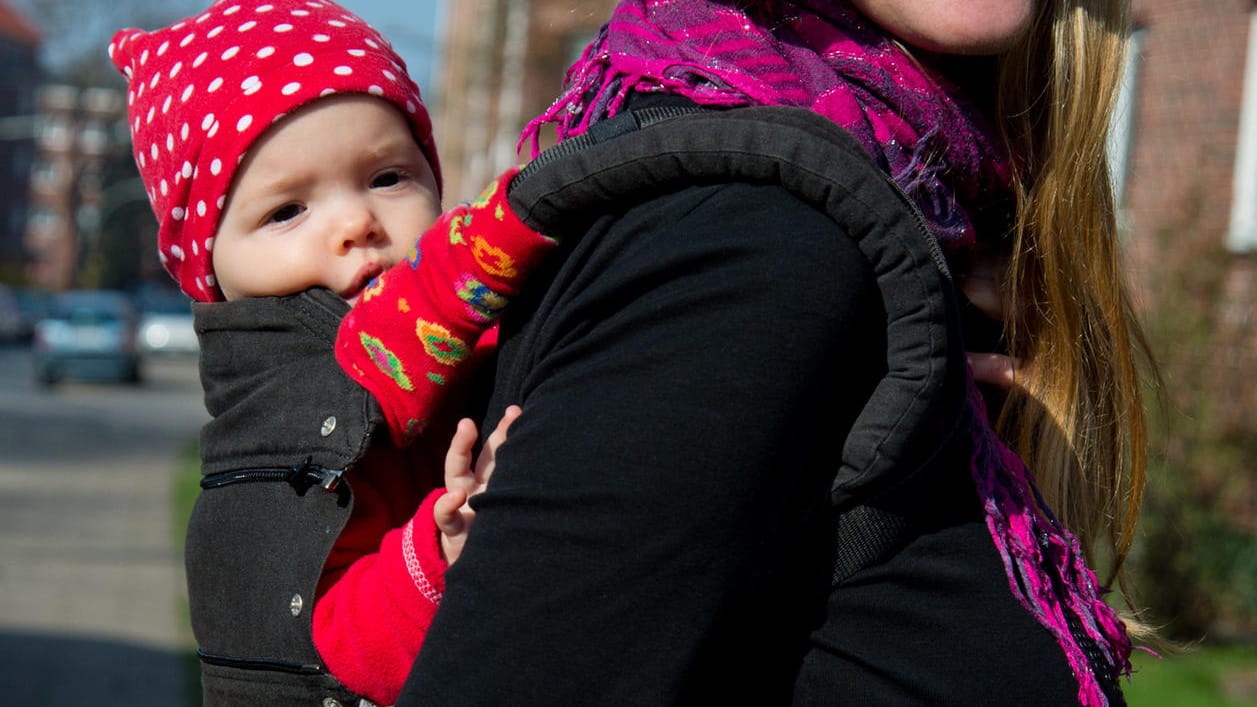 Frau mit Baby auf dem Rücken: Eine Babytrage ist eine praktische Sache. Am besten wechselt man ab: Mal sitzt das Baby vorn, mal hinten in der Trage.