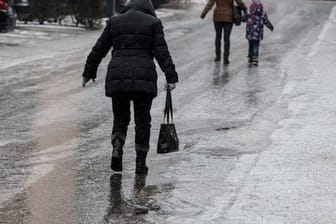 Passanten gehen vorsichtig auf einer vereisten Straße: In den kommenden Tagen ist mit Glatteis zu rechnen.