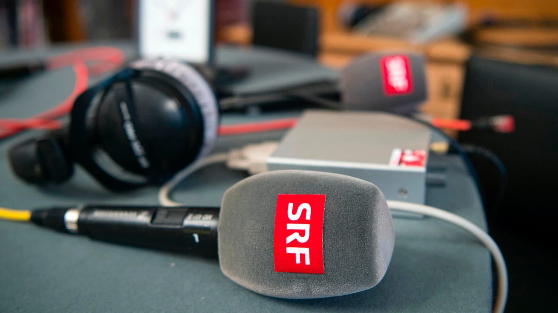 Mikrofone und ein Kopfhörer vom Schweizer Radio und Fernsehen (SRF): In einem Volksentscheid sprachen sich die Schweizer klar für die Rundfunkgebühr aus. Nun soll es im öffentlichen Rundfunk weitreichende Reformen geben. Mikrofone und ein Kopfhörer vom Schweizer Radio und Fernsehen (SRF): In einem Volksentscheid sprachen sich die Schweizer klar für die Rundfunkgebühr aus. Nun soll es im öffentlichen Rundfunk weitreichende Reformen geben.