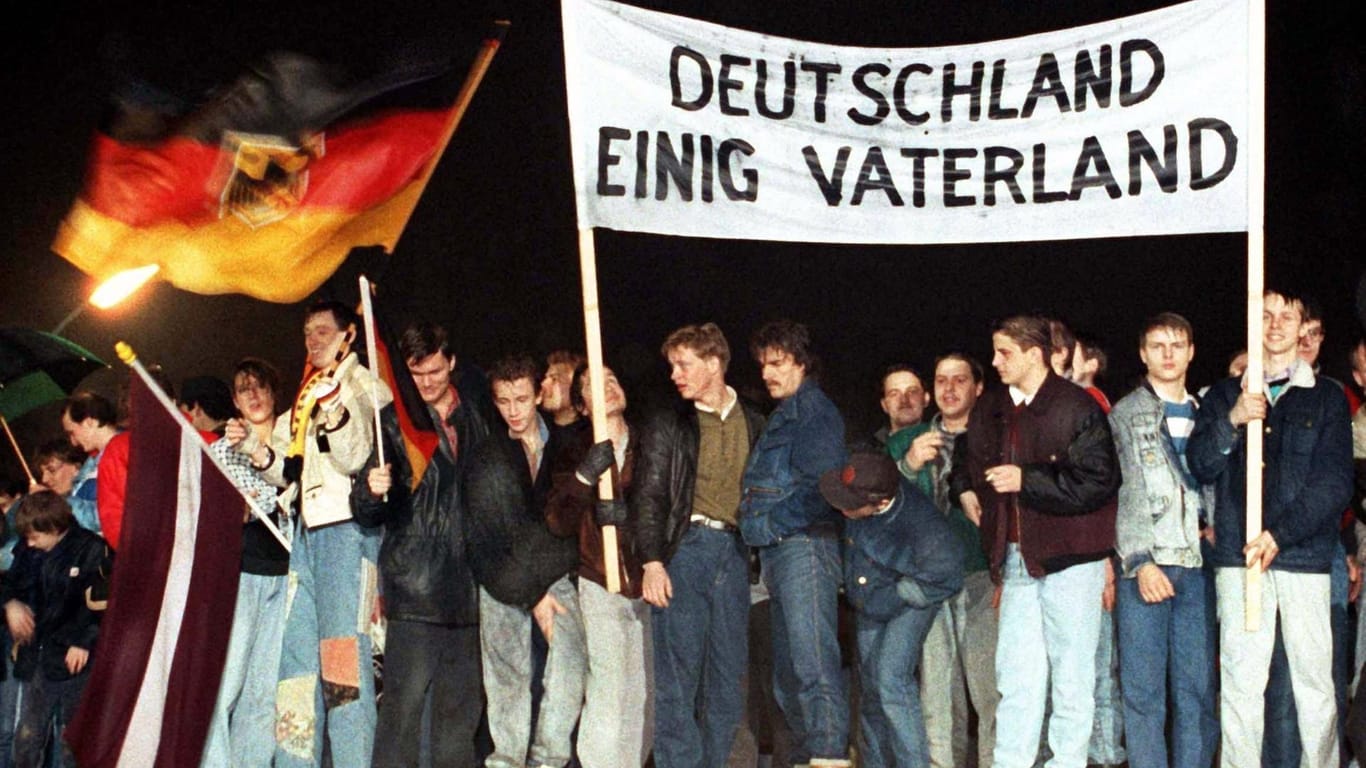Noch zeitgemäß? Menschen feiern im Dezember '89 mit "Deutschland Einig Vaterland"-Banner auf der Mauer am Brandenburger Tor in Berlin.