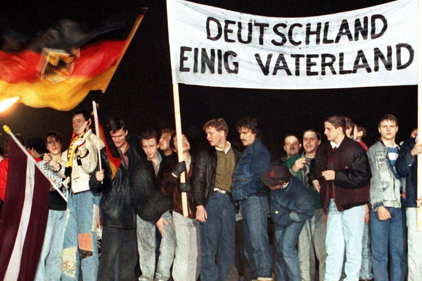 Noch zeitgemäß? Menschen feiern im Dezember '89 mit "Deutschland Einig Vaterland"-Banner auf der Mauer am Brandenburger Tor in Berlin.