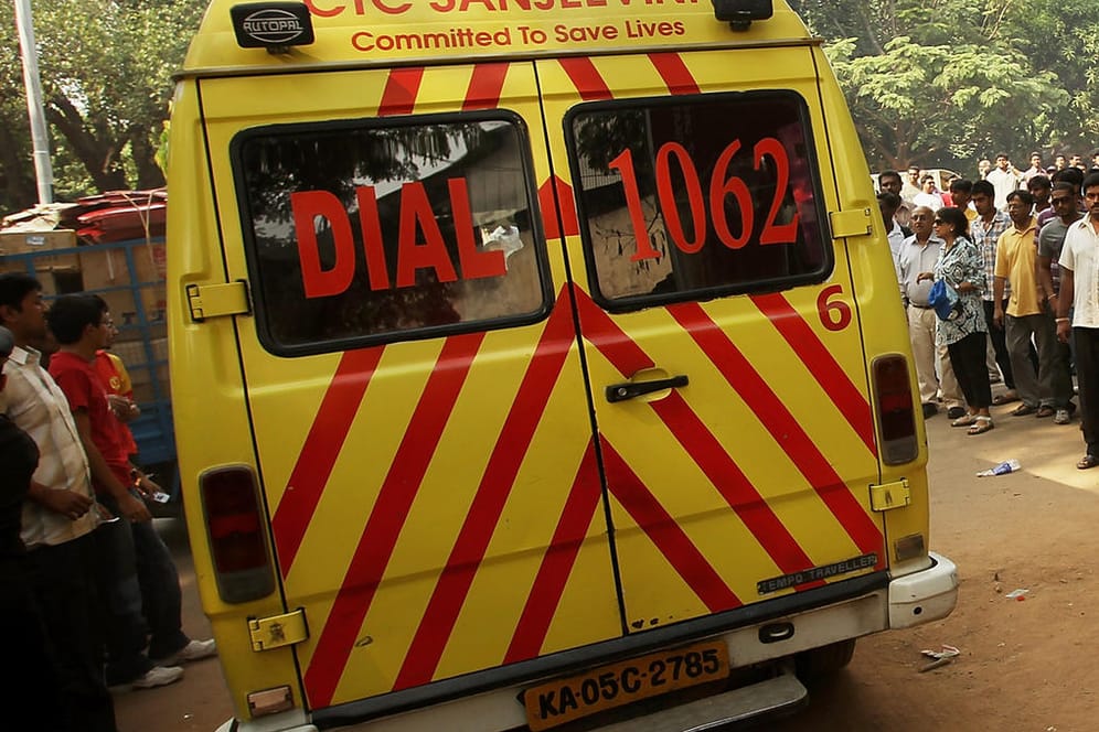 Polizist steht vor einem Krankenwagen: Mindestens 25 Tote bei Unfall von Lkw mit Hochzeitsgesellschaft in Indien.