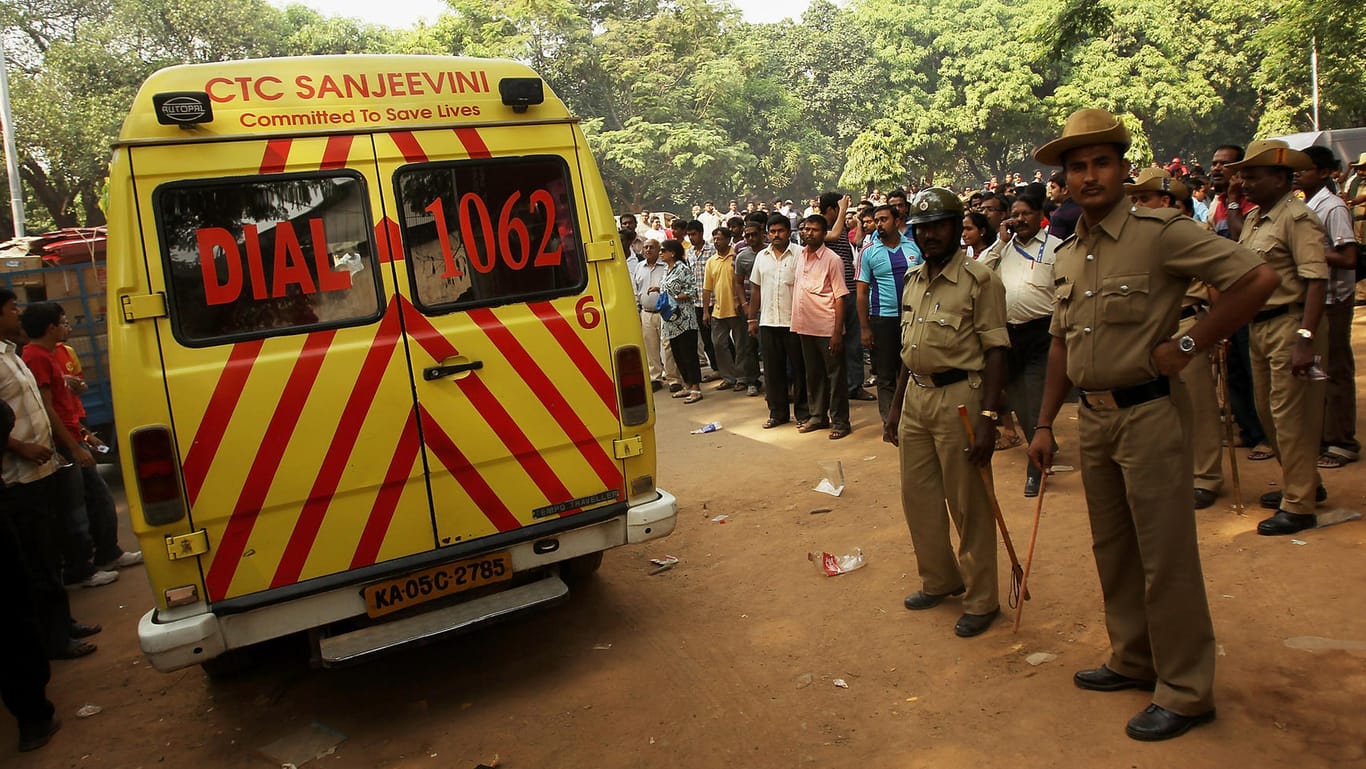 Polizist steht vor einem Krankenwagen: Mindestens 25 Tote bei Unfall von Lkw mit Hochzeitsgesellschaft in Indien.