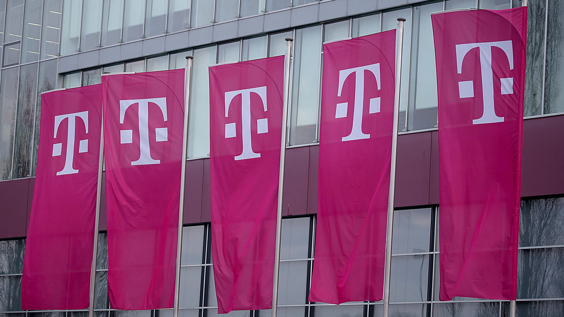 Fahnen wehen vor einem Gebäude der Deutschen Telekom in Bonn: Im Streit mit der Netzwerkagentur beharrt die Telekom auf die Rechtmäßigkeit ihres Streaming-Tarifs.