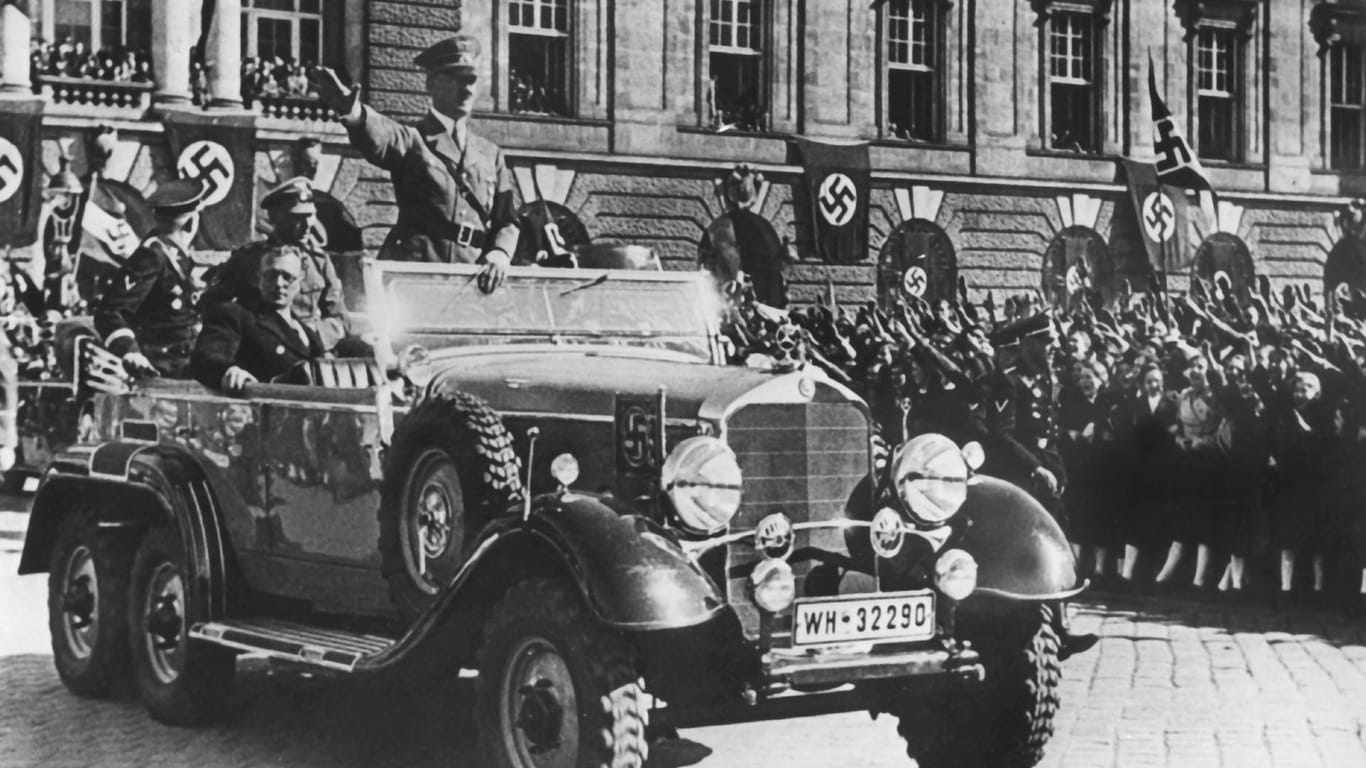 In einem Auto stehend grüßt Adolf Hitler die ihm zujubelnde Menschenmenge am 14. März 1938 in Wien (Österreich), neben ihm der österreichische Kanzler Arthur Seyss-Inquart.
