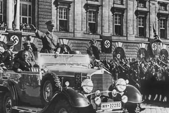 In einem Auto stehend grüßt Adolf Hitler die ihm zujubelnde Menschenmenge in Wien (Österreich) am 14. März 1938, neben ihm sitzt der österreichische Kanzler Arthur Seyss-Inquart: Am 12. März 1938 überschreiten Soldaten der deutschen Wehrmnacht die Grenze zur Alpenrepublik.