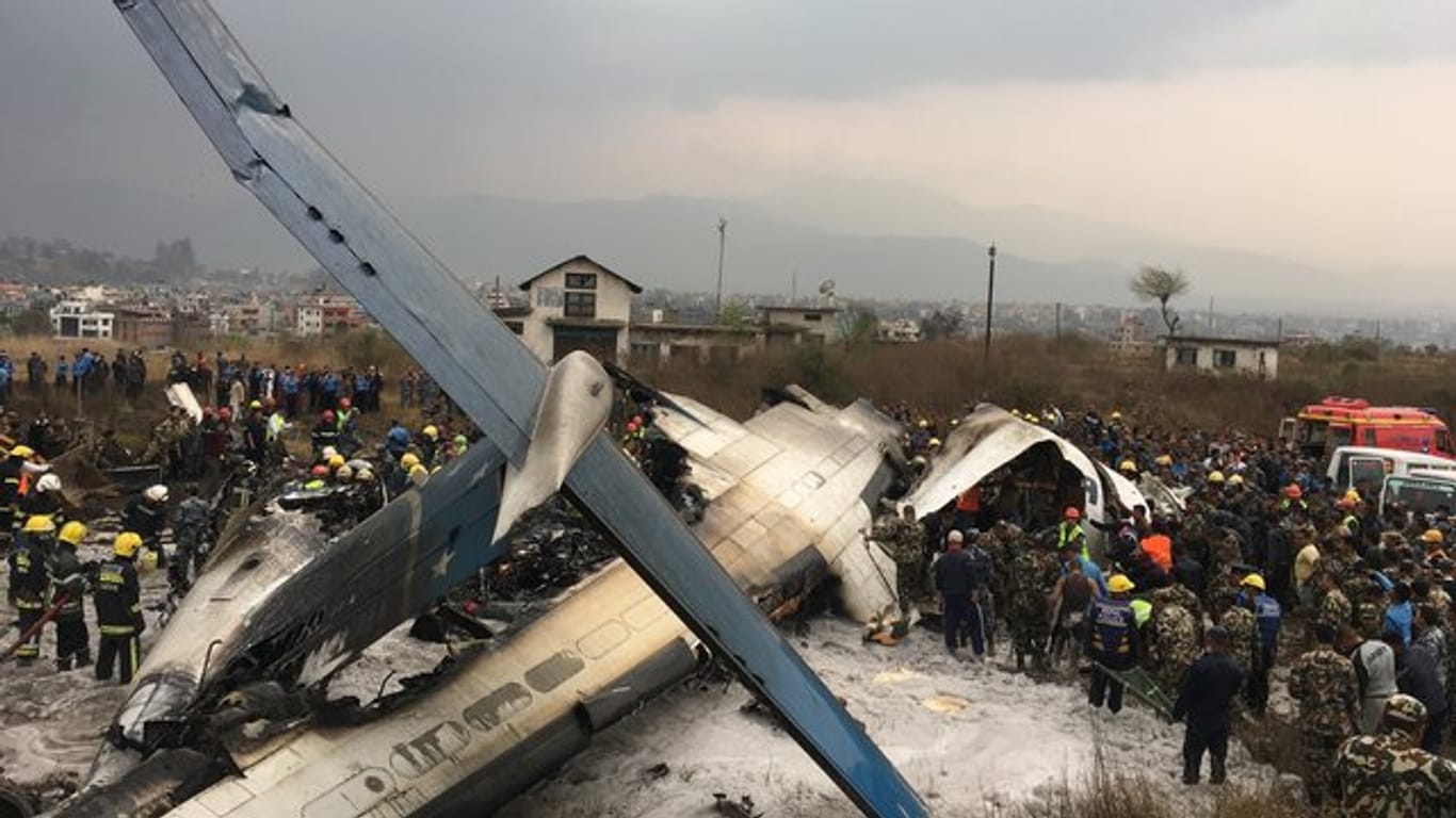Rettungskräfte stehen auf dem Flughafen von Kathmandu neben der abgestürzten Maschine.