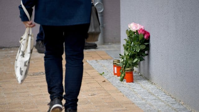 Blumen und Grablichter stehen an einem Mehrfamilienhaus.