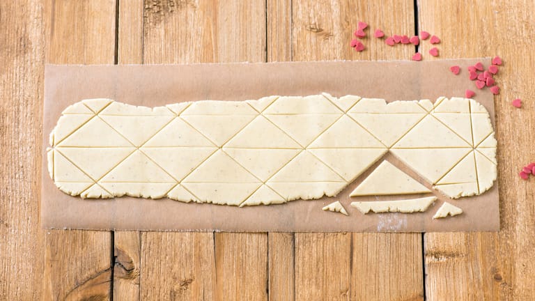 Plätzchenteig: Für die Liebesbrief-Kekse wird der Mürbetig dünn ausgerollt. Dann schneidet man Dreiecke aus.