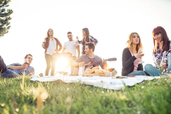 Eine Gruppe von Freunden picknickt: Forscher fanden heraus, dass Erwachsene durch die Sommerzeit im Schnitt eine halbe Stunde länger draußen ihre Freizeit genießen