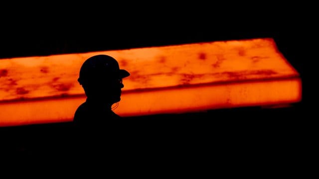 Die Silhouette eines Stahlarbeiters vor glühendem Stahl.