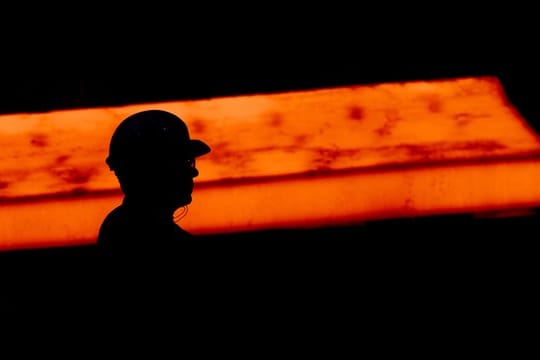 Die Silhouette eines Stahlarbeiters vor glühendem Stahl.