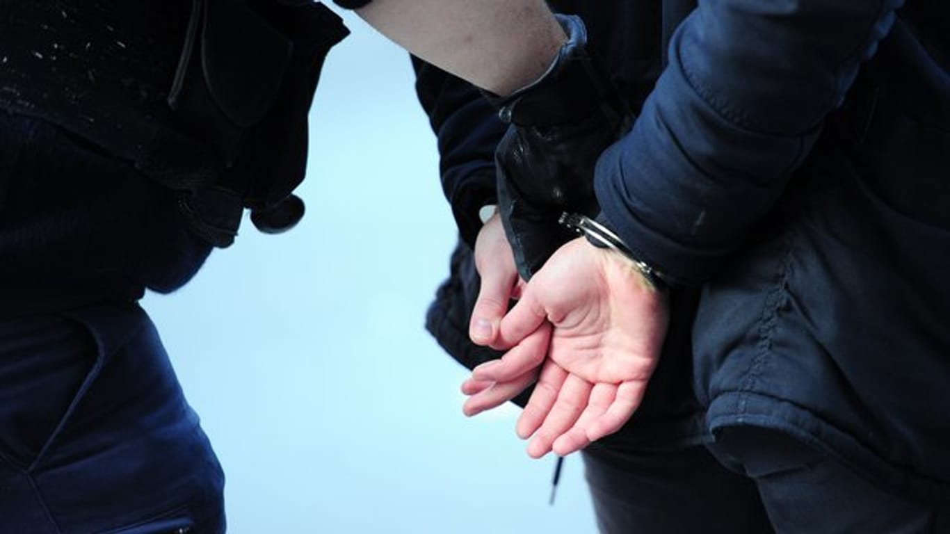 Ein Polizist führt einen mit Handschellen gefesselten Mann ab.
