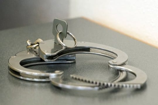 Handschellen auf einem Tisch (Symbolfoto): Nach langen Ermittlungen gegen die Betreiber von "Migrantenschreck" ist ein Verdächtiger verhaftet worden.