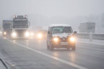 Autos und Lastwagen fahren im morgendlichen Verkehr bei Schneetreiben über die A 7.