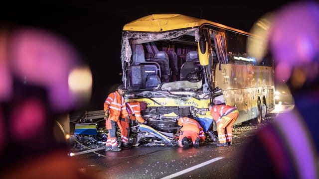 Mitarbeiter eines Abschleppunternehmens vor dem schwer beschädigten Reisebus.