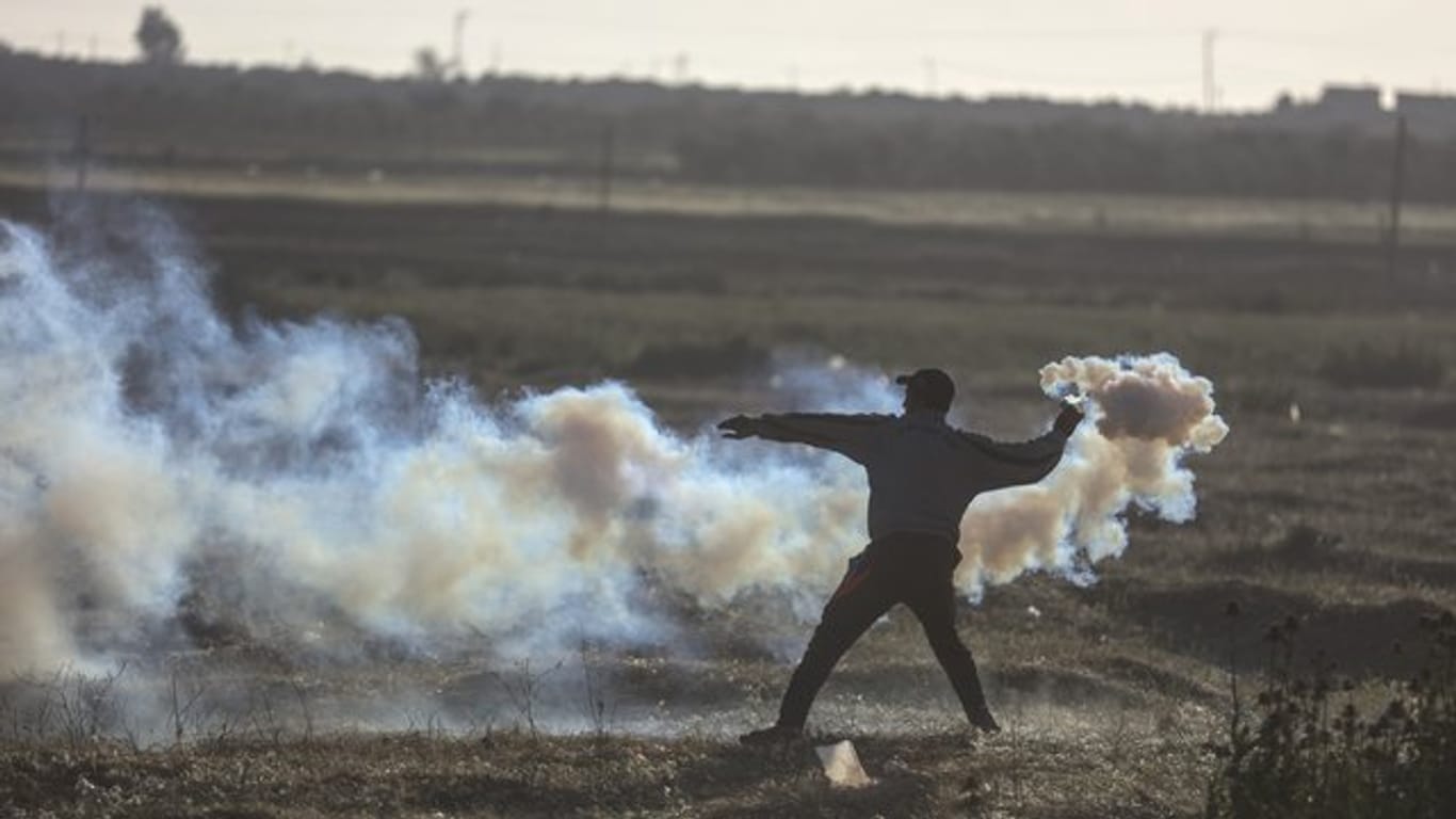 Ein Palästinenser wirft bei Zusammenstößen zwischen Demonstranten und israelischen Soldaten einen Tränengaskanister zurück Richtung Grenze.