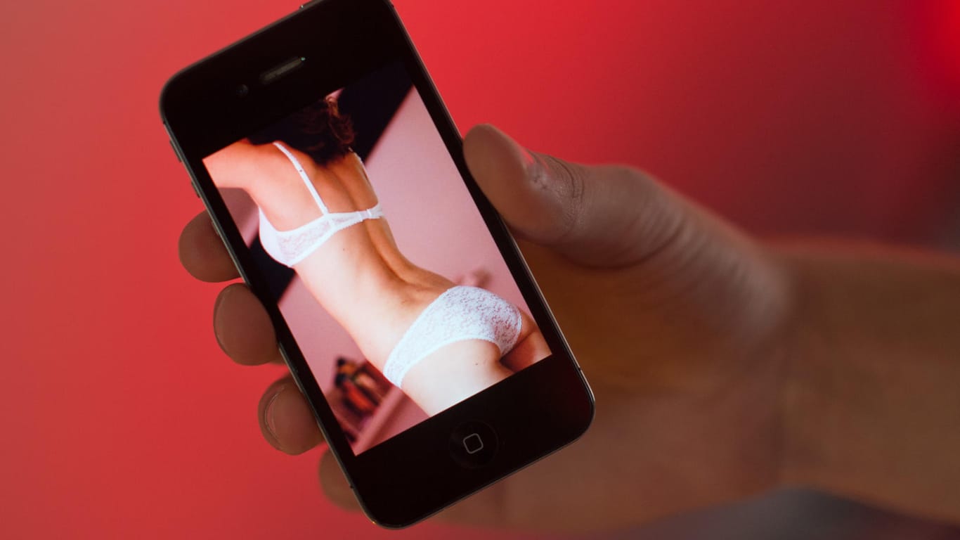 Eine Hand hält ein Smartphone, auf dem ein erotisches Foto einer Frau zu sehen ist: 72 Frauen haben bei der Polizei Wuppertal Anzeige erstattet, weil sie Nacktfoto-Montagen mit ihren Gesichtern im Netz gefunden haben. (Symbolbild)