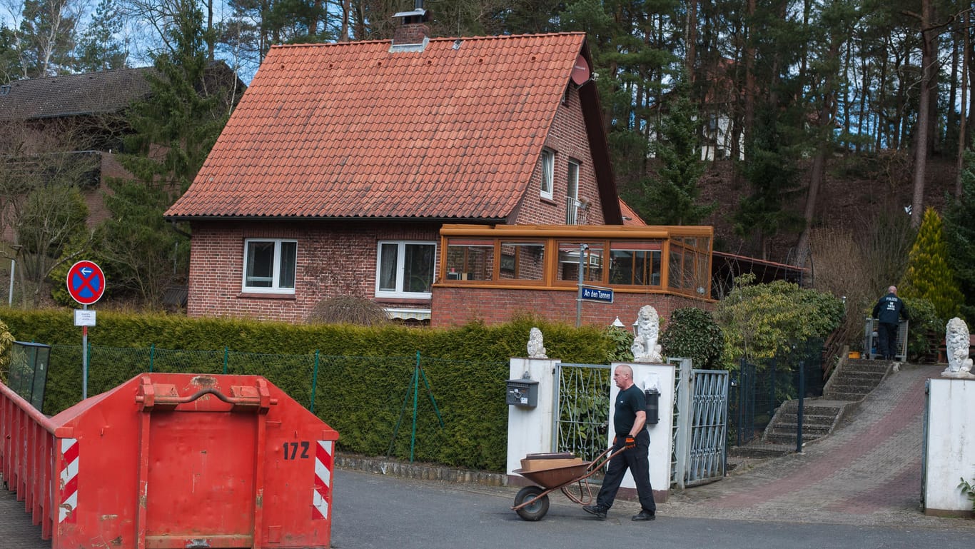 Ein Polizist fährt mit einer Schubkarre Gegenstände von einem Grundstück herunter: Auf dem ehemaligen Grundstück eines mutmaßlichen Serienmörders in Lüneburg (Niedersachsen) sucht die Polizei nach Hinweisen auf weitere Verbrechen.