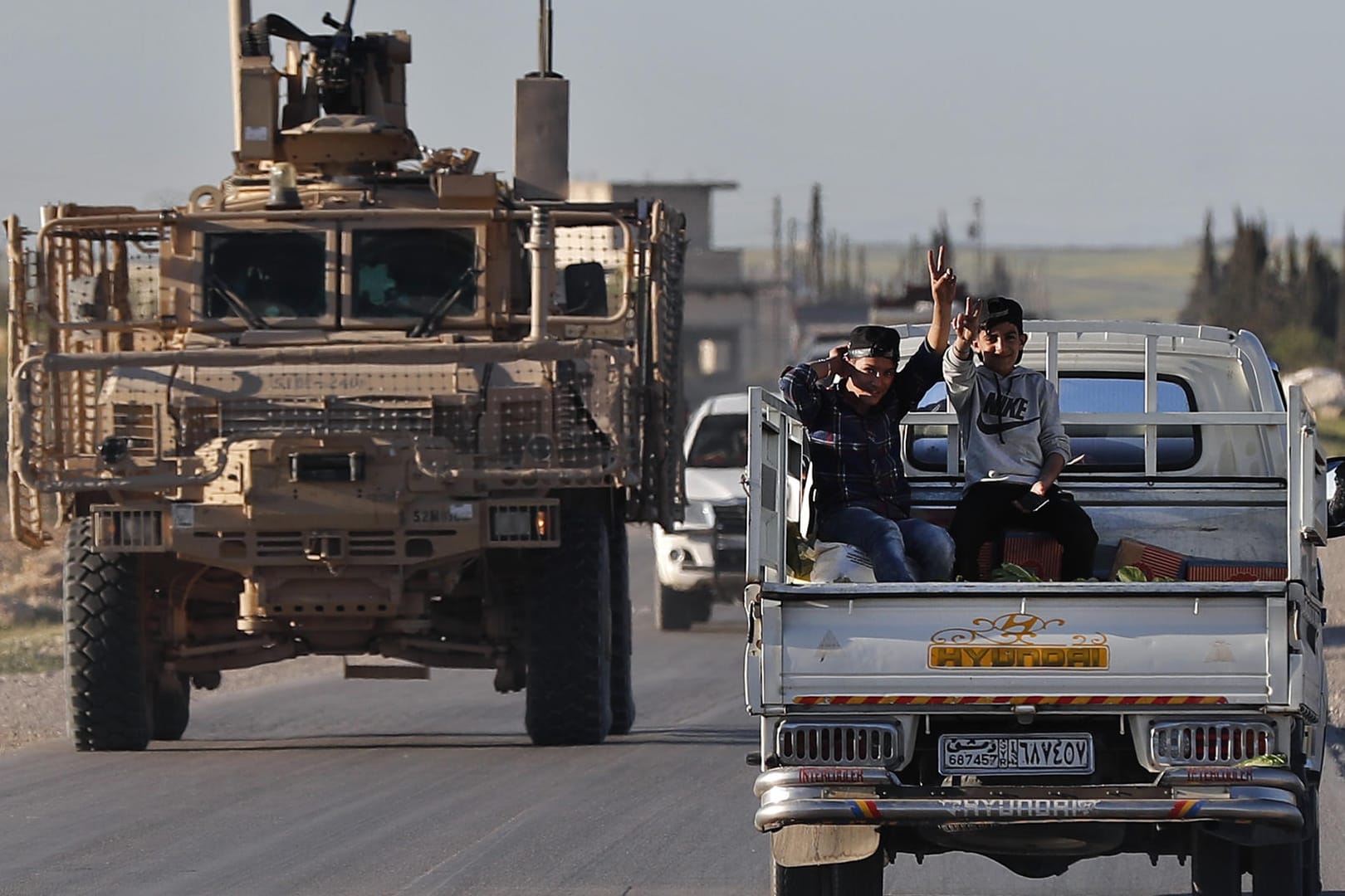 Syrische Jungen auf einem Kleintransporter in Manbidsch neben einem Fahrzeug der US-Truppen: Die USA werden vorerst weiter im Bürgerkriegsland bleiben.