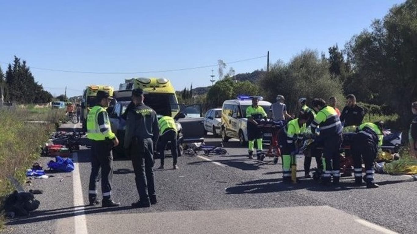Rettungskräfte und Polizisten der Guardia Civil stehen am Unfallort, an dem ein Auto in die Radfahrergruppe fuhr.