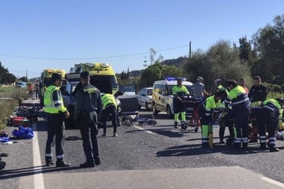 Rettungskräfte und Polizisten der Guardia Civil stehen am Unfallort, an dem ein Auto in die Radfahrergruppe fuhr.