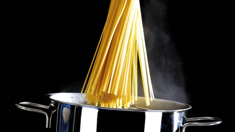 Spaghetti werden in einen Kochtopf gegeben.