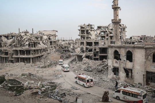 Fahrzeuge des Syrischen Roten Halbmonds fahren in Ost-Ghuta an völlig zerstörten Häusern vorbei.
