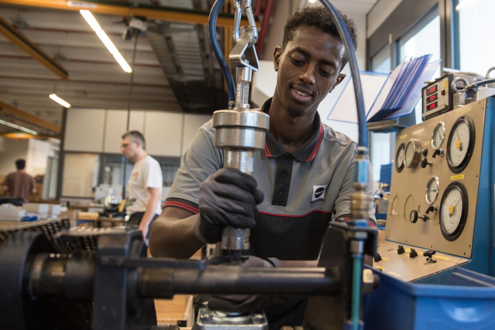 Abdisamed Abdullahi Mohamoud (19, aus Somalia) an einem Prüfstand für Regelventile: Industrie und handwerk fordern bessere Sprachbildung für Flüchtlinge in Deutschland.