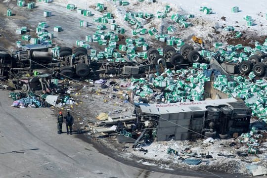 Helfer stehen neben Trümmern und den zwei Fahrzeugwracks am Unfallort, an dem bei einem Busunglück zahlreiche Menschen ums Leben gekommen sind.