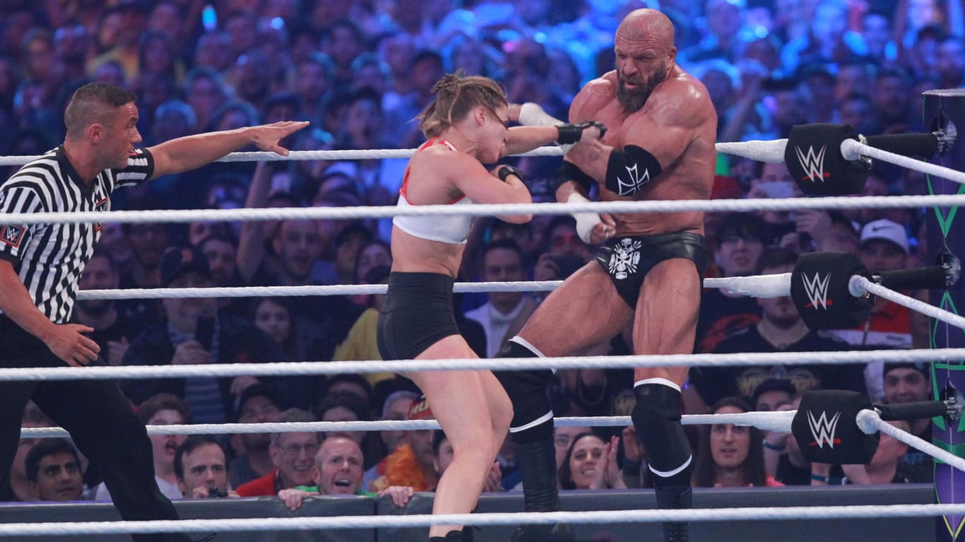 Ronda Rousey (m.) schlägt auf Triple H ein.