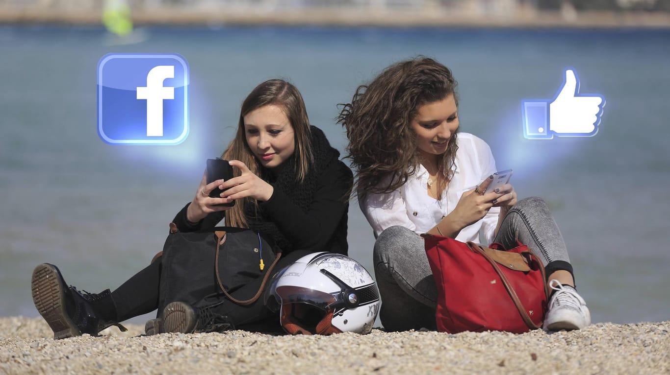 Zwei Teenager sitzen am Strand und posten auf Facebook