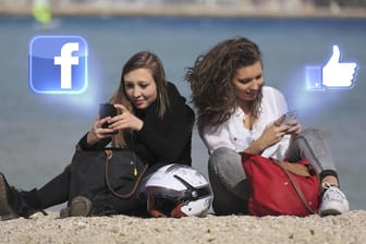 Zwei Teenager sitzen am Strand und posten auf Facebook