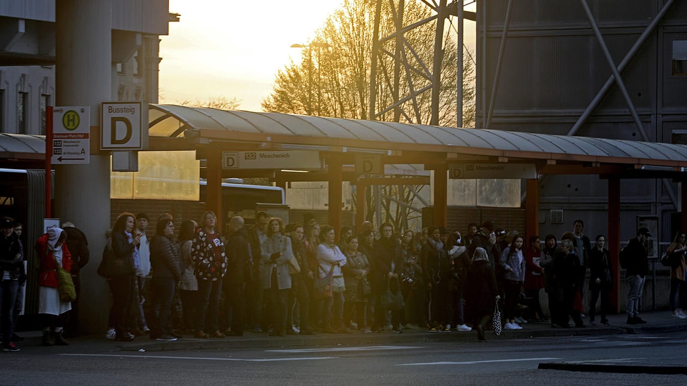 Dutzende Fahrgäste stehen an einer Haltestelle in Köln, an der einer der wenigen Buslinien die bedient werden, abfährt.