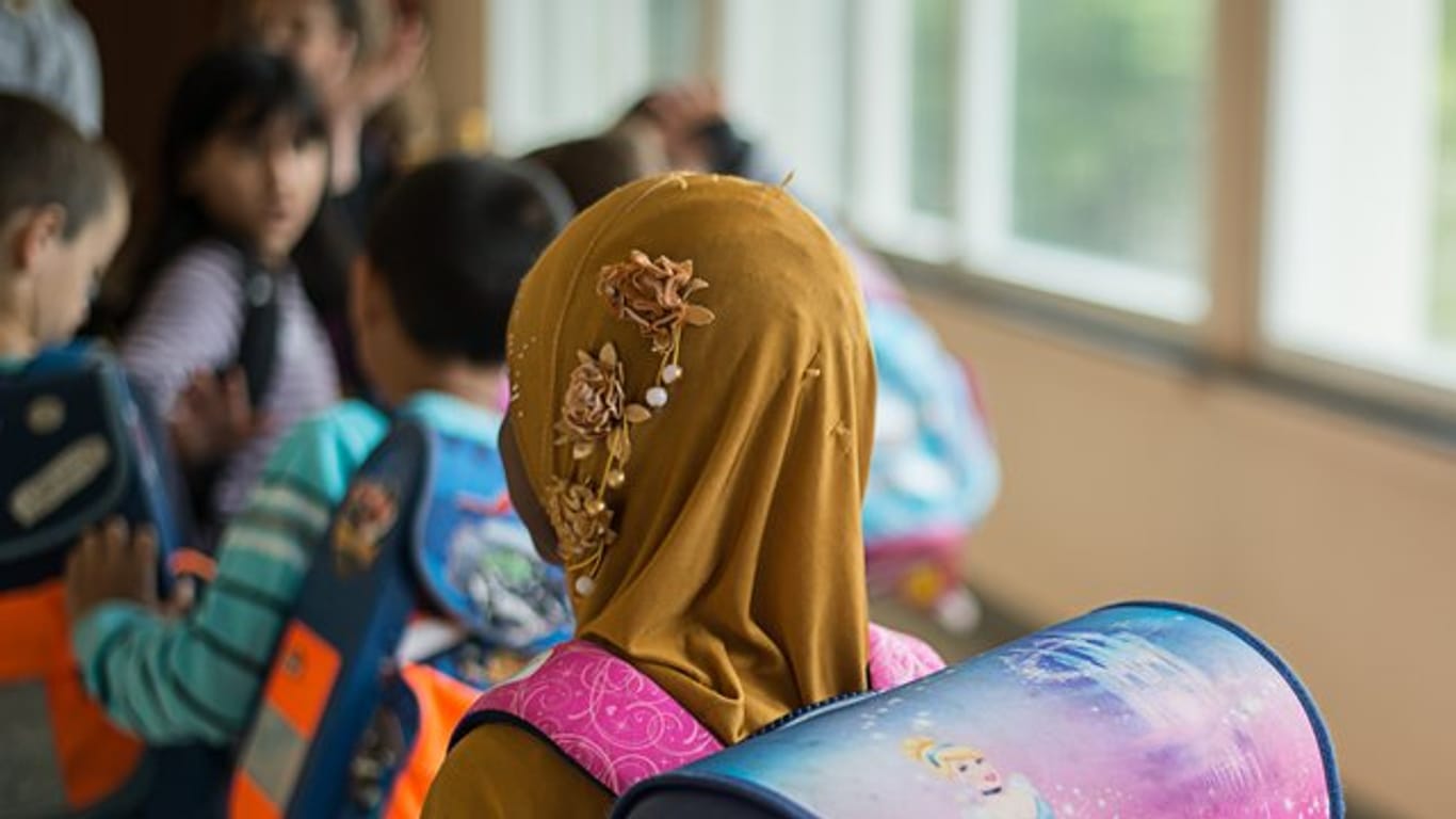 Ein Mädchen mit Kopftuch steht vor einem Klassenzimmer.