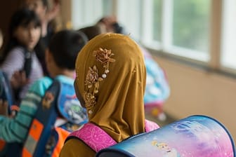 Ein Mädchen mit Kopftuch steht vor einem Klassenzimmer.