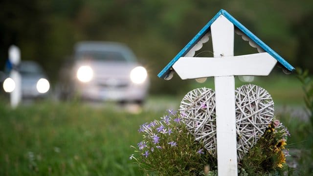 Autos fahren an einem weißen Kreuz für eine Unfalltote vorbei. Autos fahren an einem weißen Kreuz für eine Unfalltote vorbei.