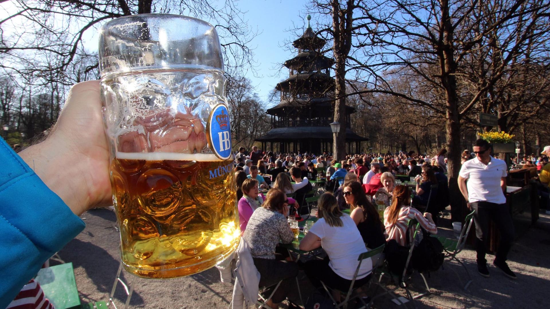 Hand mit Maß Bier im voll besetzten Biergarten am Chinesischen Turm