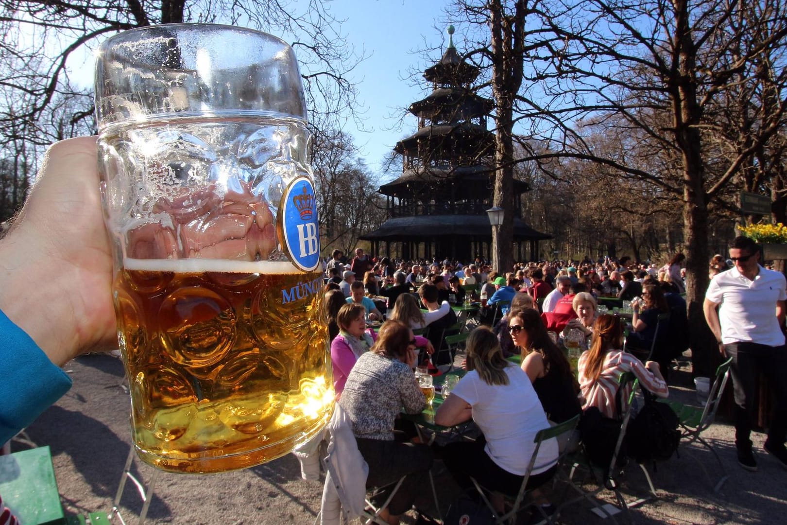 Hand mit Maß Bier im voll besetzten Biergarten am Chinesischen Turm