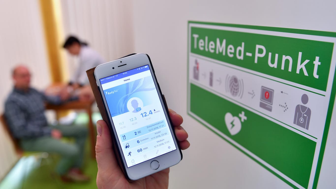 Digitalisierung beim Arzt: Eine Sozialarbeiterin misst Blutdruckwerte eines Patienten und übermittelt diese drahtlos per Smartphone an einen Arzt.