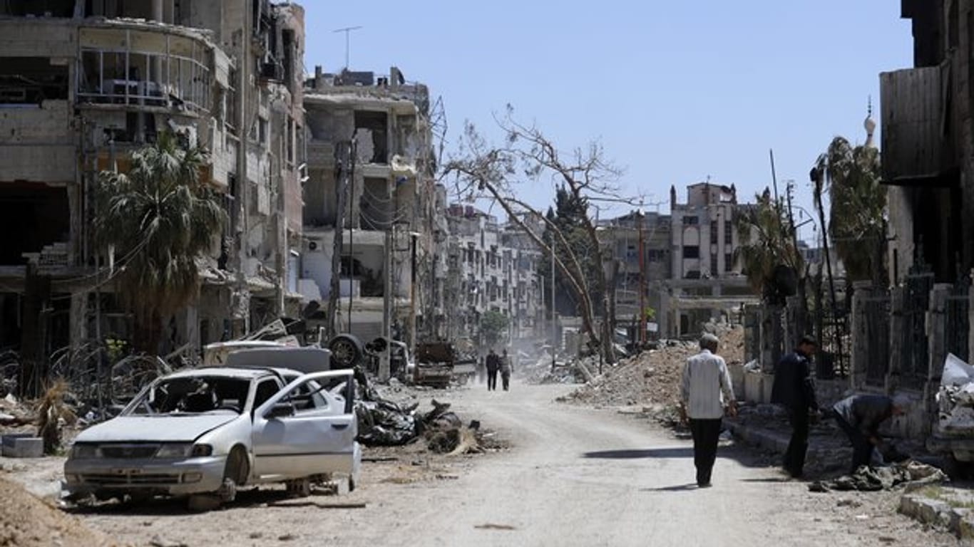 Menschen gehen an zerstörten Häusern und Autos im syrischen Duma vorbei.