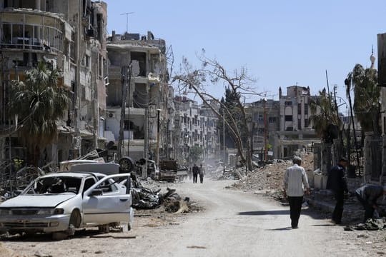 Menschen gehen an zerstörten Häusern und Autos im syrischen Duma vorbei.