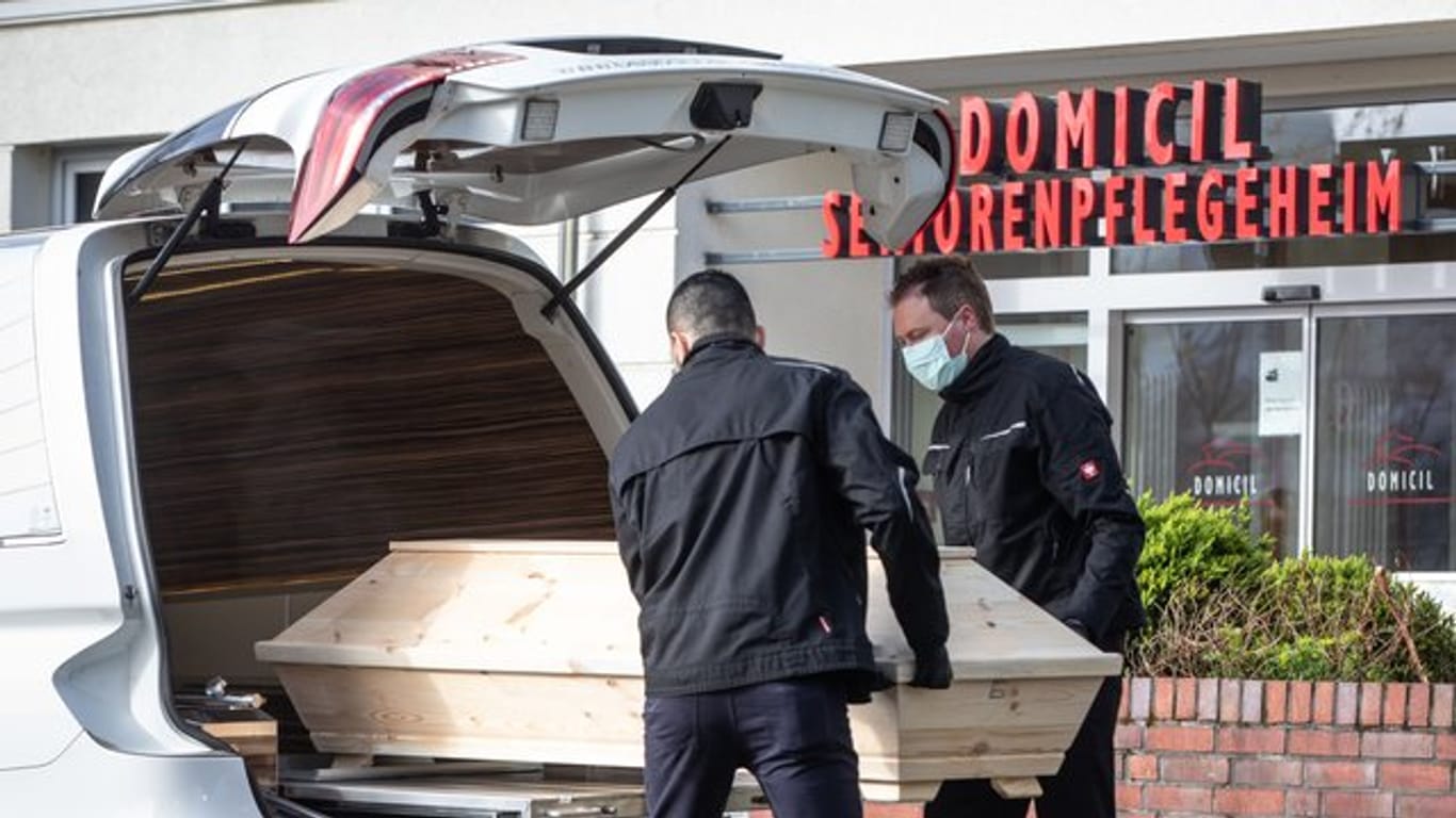 Mitarbeiter eines Bestattungsinstituts heben den Sarg des Todesopfers in ihr Fahrzeug.