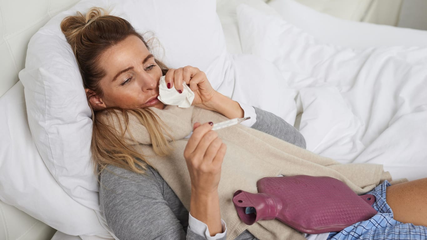 Kranke Frau im Bett guckt auf Fieberthermometer