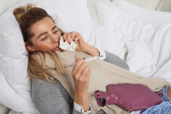 Kranke Frau im Bett guckt auf Fieberthermometer