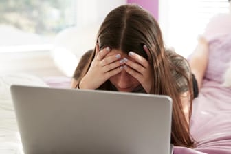 Trauriges Mädchen vorm Laptop: Auslöser für digitales Selbstmobbing können Einsamkeit und Traurigkeit sein.