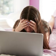 Trauriges Mädchen vorm Laptop: Auslöser für digitales Selbstmobbing können Einsamkeit und Traurigkeit sein.
